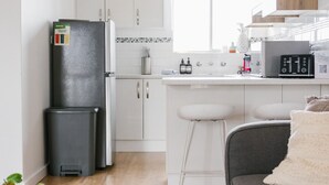 Een moderne keuken met witte kasten, een zwarte koelkast en een magnetron. Er is een klein barretje met krukjes.