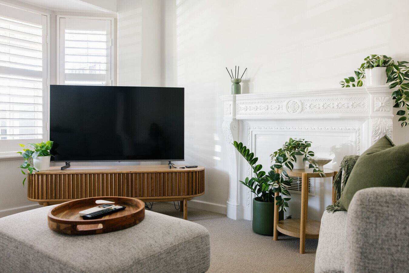 Ett vardagsrum med en platt-TV placerad på en träkonsol, en öppen spis och krukväxter.