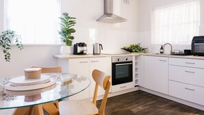 Une cuisine moderne avec des armoires blanches, une table en verre et une hotte de cuisinière en acier inoxydable.