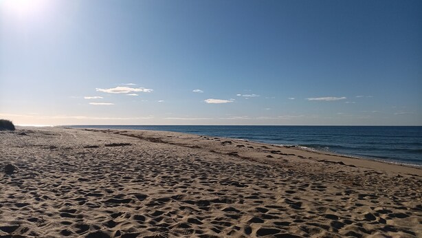 Ein Strand mit Sand und Wasser, ein klarer Himmel und vereinzelte Wolken.