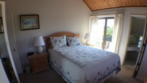 Ein Schlafzimmer mit einem Bett, zwei Nachttischen, einem Schranken und einem Holz-Kopfteil sowie einem Fenster mit Vorhängen.