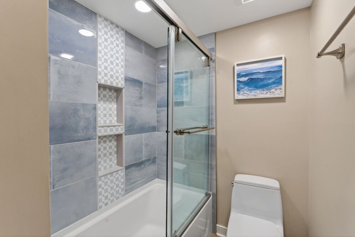 A bathroom with a glass-enclosed shower, a toilet, and a wall-mounted shelf with patterned tiles.