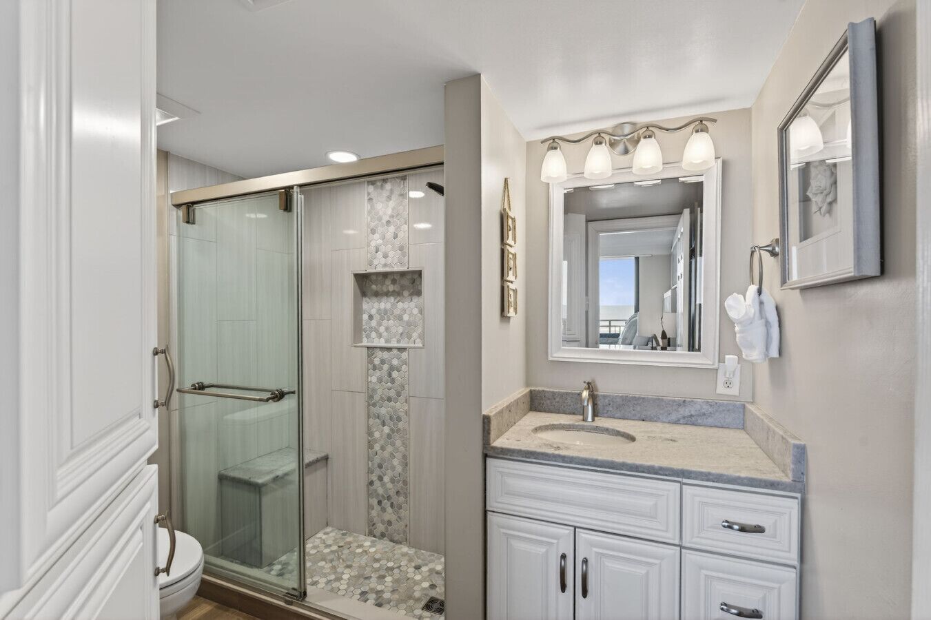 A bathroom with a glass shower enclosure, a vanity with a sink, and a large mirror.