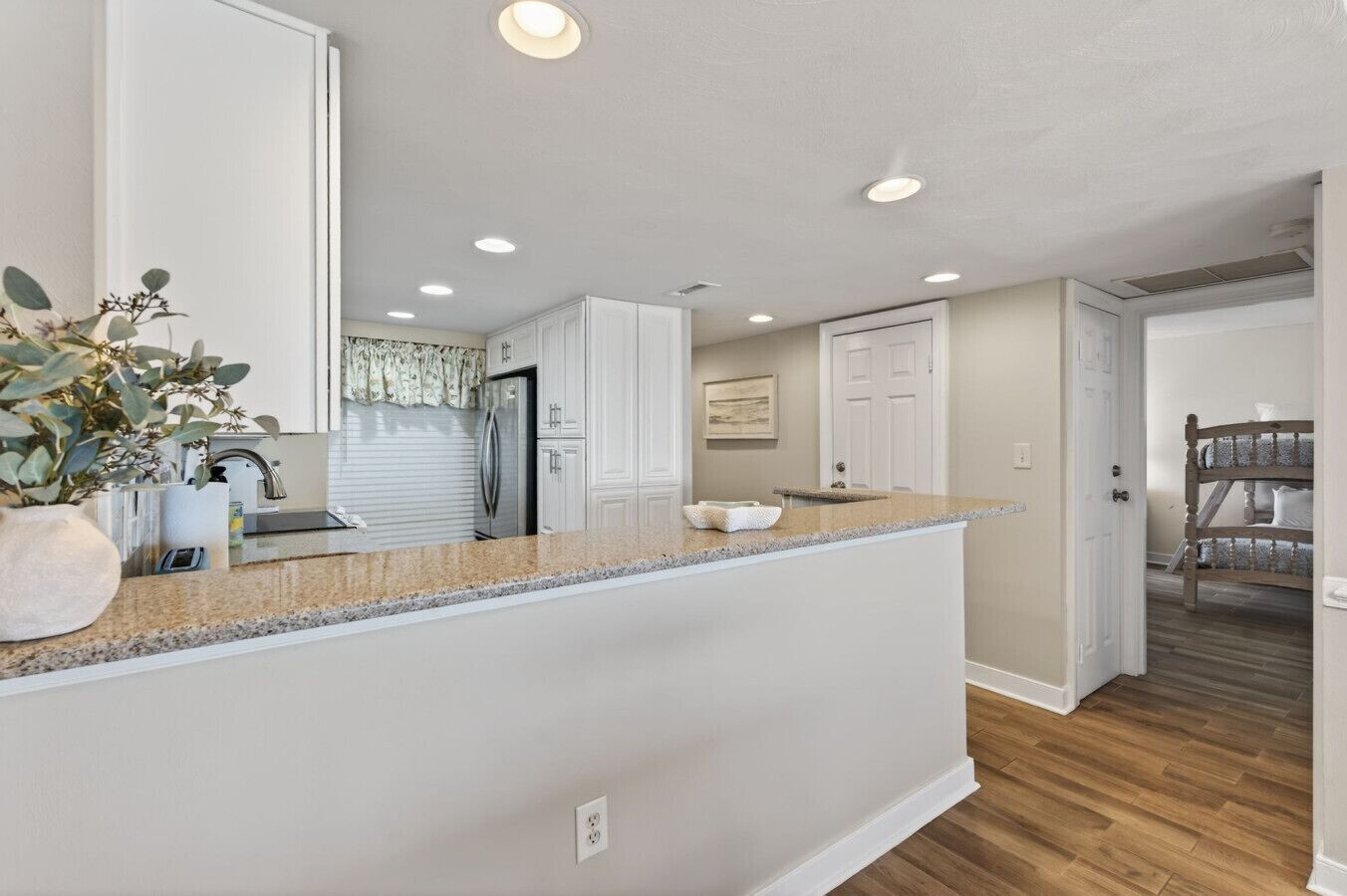 A modern kitchen with a granite countertop, white cabinetry, and a built-in refrigerator.