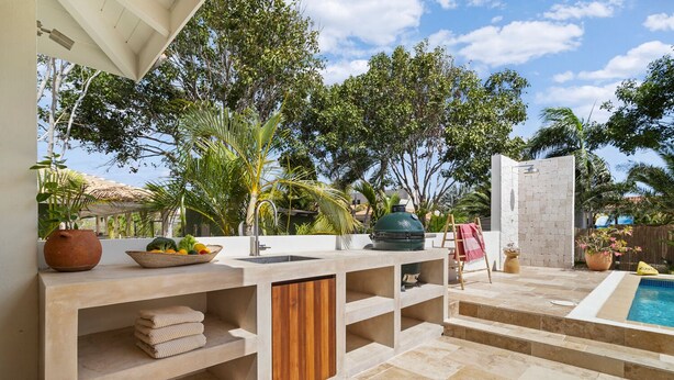 Une cuisine extérieure moderne, dotée d’un évier encastré, d’un barbecue et d’un espace aménagé au bord de la piscine, avec des marches menant à celle-ci.