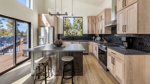 A modern kitchen with a large island, wooden cabinets, and a view of the outdoors. - Hilltop Luxury with Terry Peak Views, Resort Amenities & Year-Round Pool (Lead)