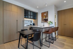 A modern kitchen with wooden cabinets, a black countertop, and bar stools. - Queensbridge Luxe River Suite. Heated Pool, Gym, Sauna, Steam, Bar, beside Crown (Southbank)