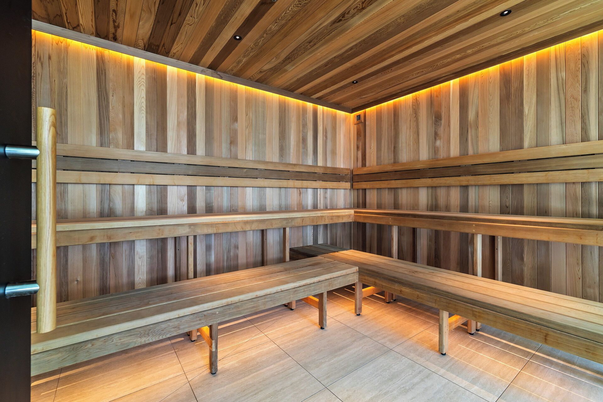 Eine Sauna mit hölzernen Bänken und schmalen Holzlatten, beleuchtet durch warmes Licht.