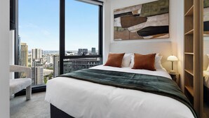 Ein modernes Hotelzimmer mit einem großen Bett, Blick auf die Stadt, einem zeitgenössischen Kunstwerk und einem Nachttisch aus Holz.