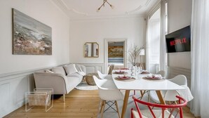 A modern living room with a white sofa, a dining table with chairs, a TV displaying 'NETFLIX,' and artwork on the walls. - 3BR in Gamla Stan by the Royal Palace (Stockholm)