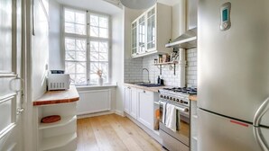 A kitchen with white cabinets, a stove, a refrigerator, and a window with a view. - 3BR in Gamla Stan by the Royal Palace (Stockholm)