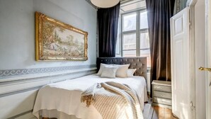 A bedroom with a bed, a large framed painting, a window with curtains, and a door. - 3BR in Gamla Stan by the Royal Palace (Stockholm)