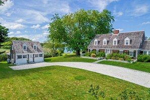 A two-story house with a large lawn and a driveway leading to the entrance. - Timeless charm at this unique waterfront compound, sleeping 14. (West Dennis)