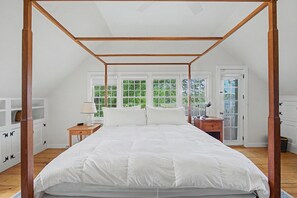A bedroom with a four-poster bed, wooden flooring, and large windows with a view of greenery. - Timeless charm at this unique waterfront compound, sleeping 14. (West Dennis)