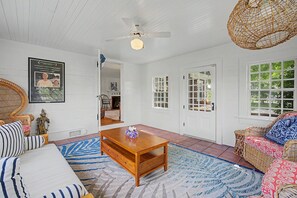 A room with a ceiling fan, a wooden coffee table, a wicker sofa, and a patterned rug. - Timeless charm at this unique waterfront compound, sleeping 14. (West Dennis)