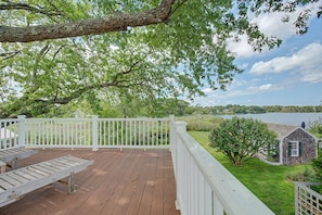 A wooden deck with white railings overlooking a lake, a grassy area, and a small building with green shutters. - Timeless charm at this unique waterfront compound, sleeping 14. (West Dennis)