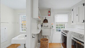 Et lille køkken med vask, vaskemaskine og et vindue med persienner.