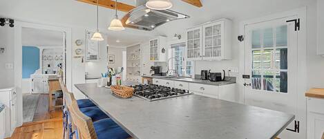 A modern kitchen with a central island, pendant lighting, and a view to the outside.