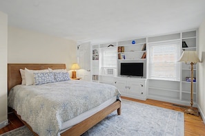 A bedroom with a bed, a TV, built-in shelves, and a window with blinds. - Timeless charm at this unique waterfront compound, sleeping 14. (West Dennis)