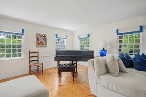 A room with a piano, a wooden chair, a sofa, and a lamp. - Timeless charm at this unique waterfront compound, sleeping 14. (West Dennis)