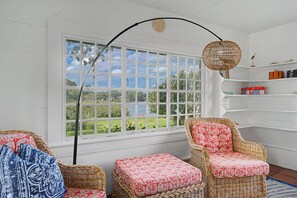 A room with a large window, wicker furniture, and a bookshelf. - Timeless charm at this unique waterfront compound, sleeping 8. (West Dennis)