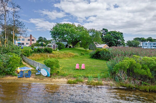 Une propriété située au bord de la rivière, avec une pelouse verdoyante, deux fauteuils Adirondack roses et un petit abri de jardin.
