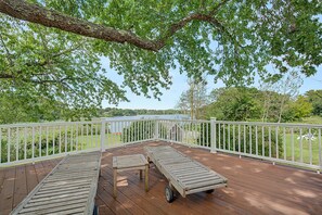 A wooden deck with a table and two lounge chairs, overlooking a lake with a white railing. - Timeless charm at this unique waterfront compound, sleeping 8. (West Dennis)
