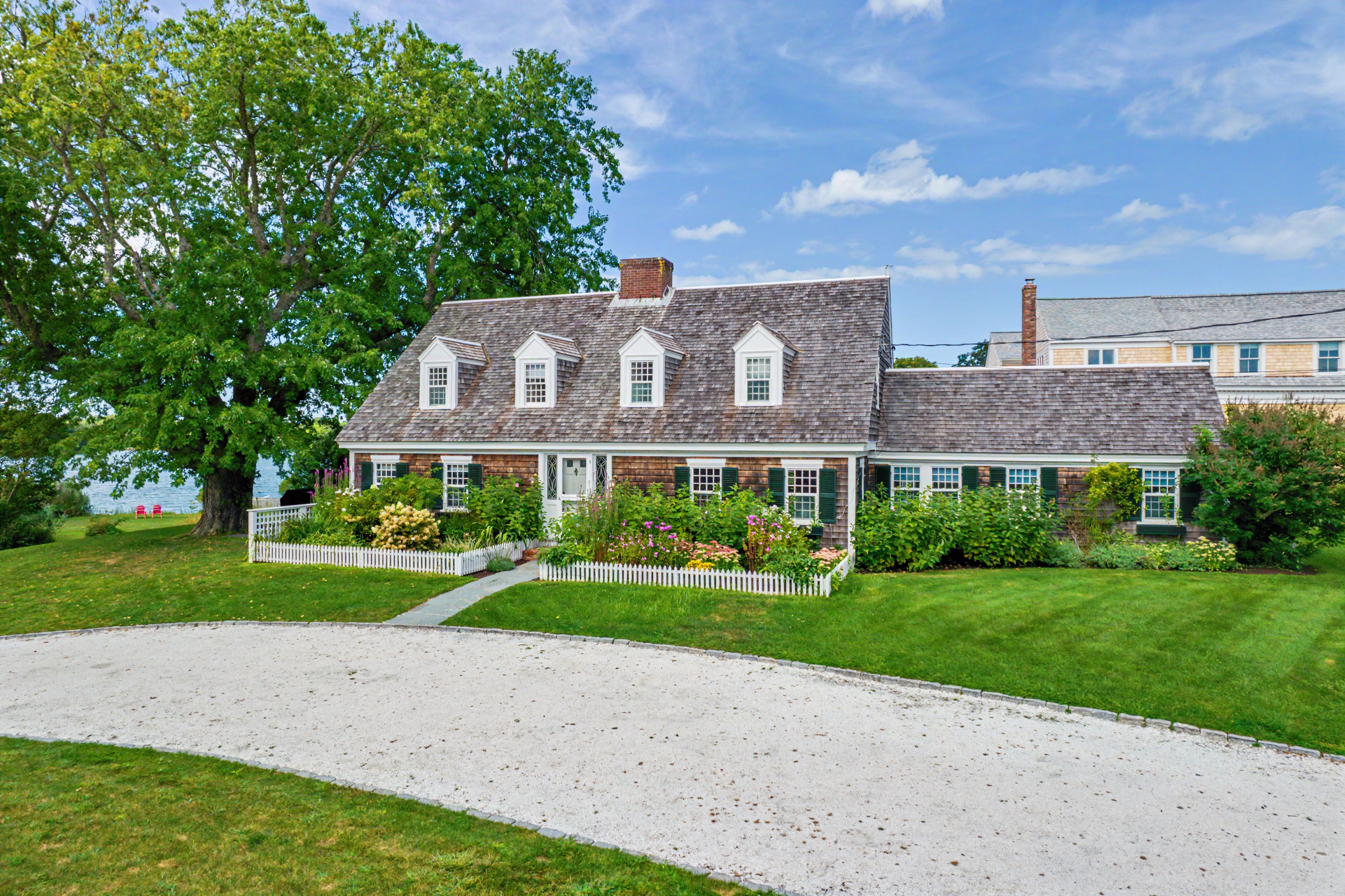 A two-story house with a white picket fence, a gravel driveway, and a well-maintained lawn.