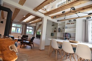 A modern interior with a wooden staircase, a dining area with white chairs, and a bookshelf filled with books. - A listed captain's house on a garden lot close to ground level (Wieck auf Darß)