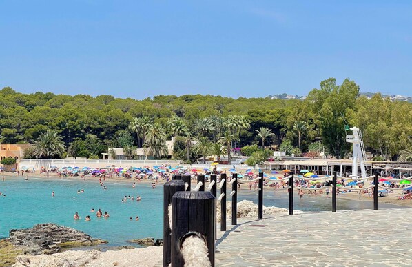 A beach with people swimming and sunbathing, a lifeguard tower, and a row of umbrellas. - Villa with private pool for 8 people – CASA SUSAN (Moraira)