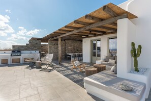 Eine Terrasse im Freien mit Steinböden, einer Holzpergola, Sitzbereichen, einem Grill und einer Kakteepflanze.