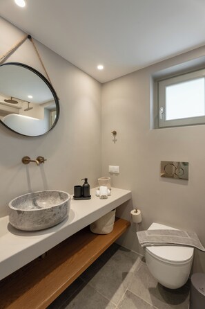 Ein modernes Badezimmer mit einem мраморный Waschbecken, einem runden Spiegel, einer Toilette und einem Fenster.