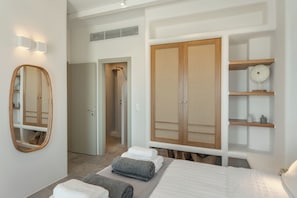 Ein modernes Schlafzimmer mit einem Bett, einem Kleiderschrank, einem Spiegel und einem Regal mit Dekoration.
