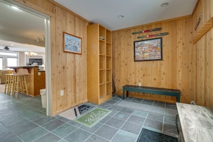 Una habitación con paneles de madera, un banco, un estante, una puerta y un felpudo.