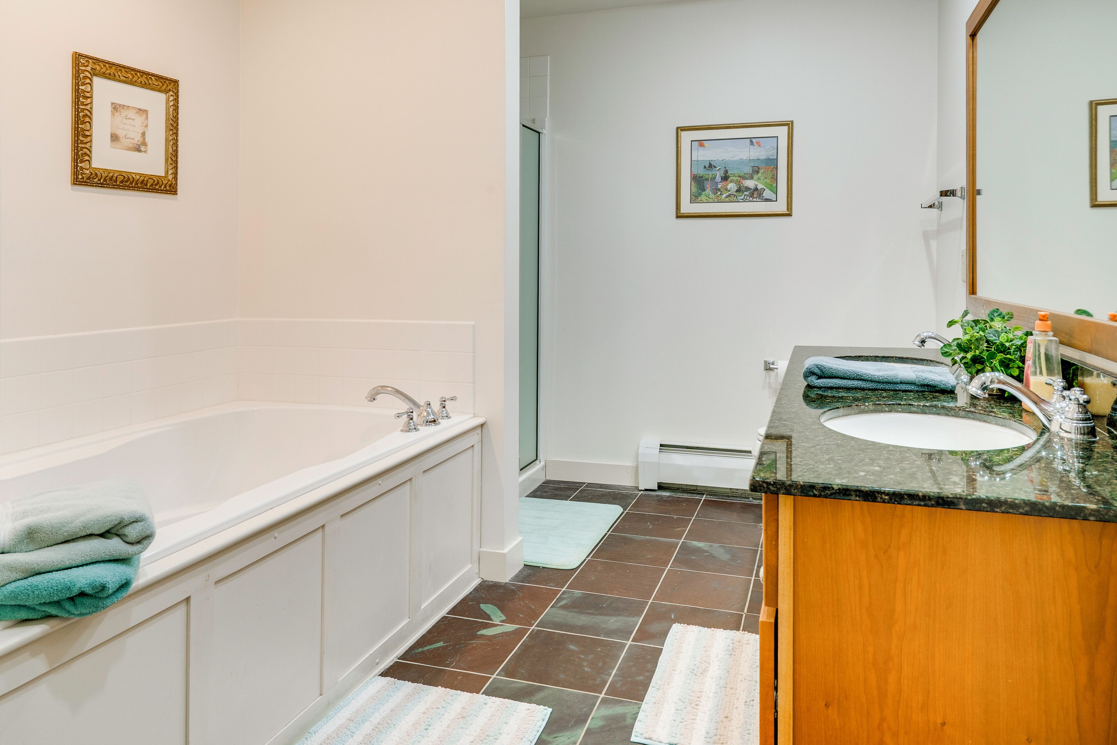 A bathroom with a bathtub, sink, and a mirror. There are towels on the tub and a framed picture on the wall.