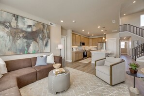 A modern living room with a sectional sofa, a round ottoman, and a large abstract painting. - Elevated Home in North Colorado Springs w/ Patio (Colorado Springs)