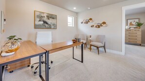 Een moderne kantoorruimte met een bureau, stoelen, een glazen tafel en een muur met abstracte kunst en decoratieve objecten.