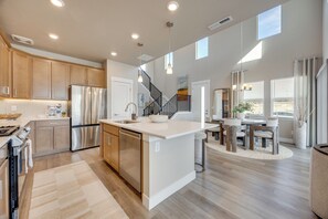 A spacious kitchen with modern appliances, a central island, and a staircase leading to an upper level. - Elevated Home in North Colorado Springs w/ Patio (Colorado Springs)