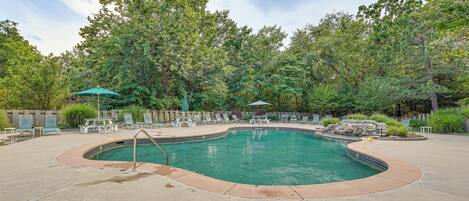 A swimming pool with a curved edge, surrounded by lounge chairs and umbrellas.