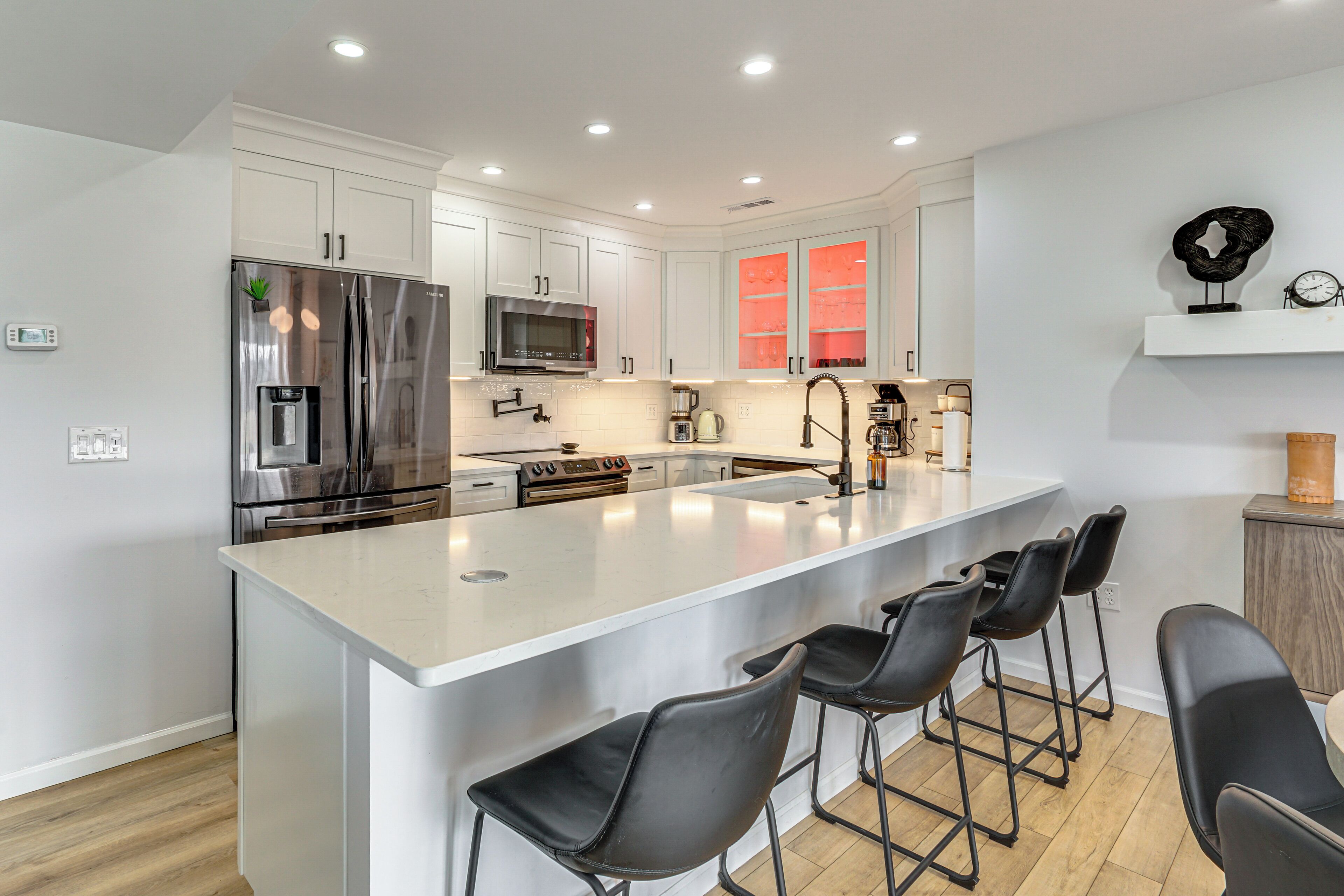 A modern kitchen with white cabinetry, stainless steel appliances, a central island with bar stools, and a microwave above the island.