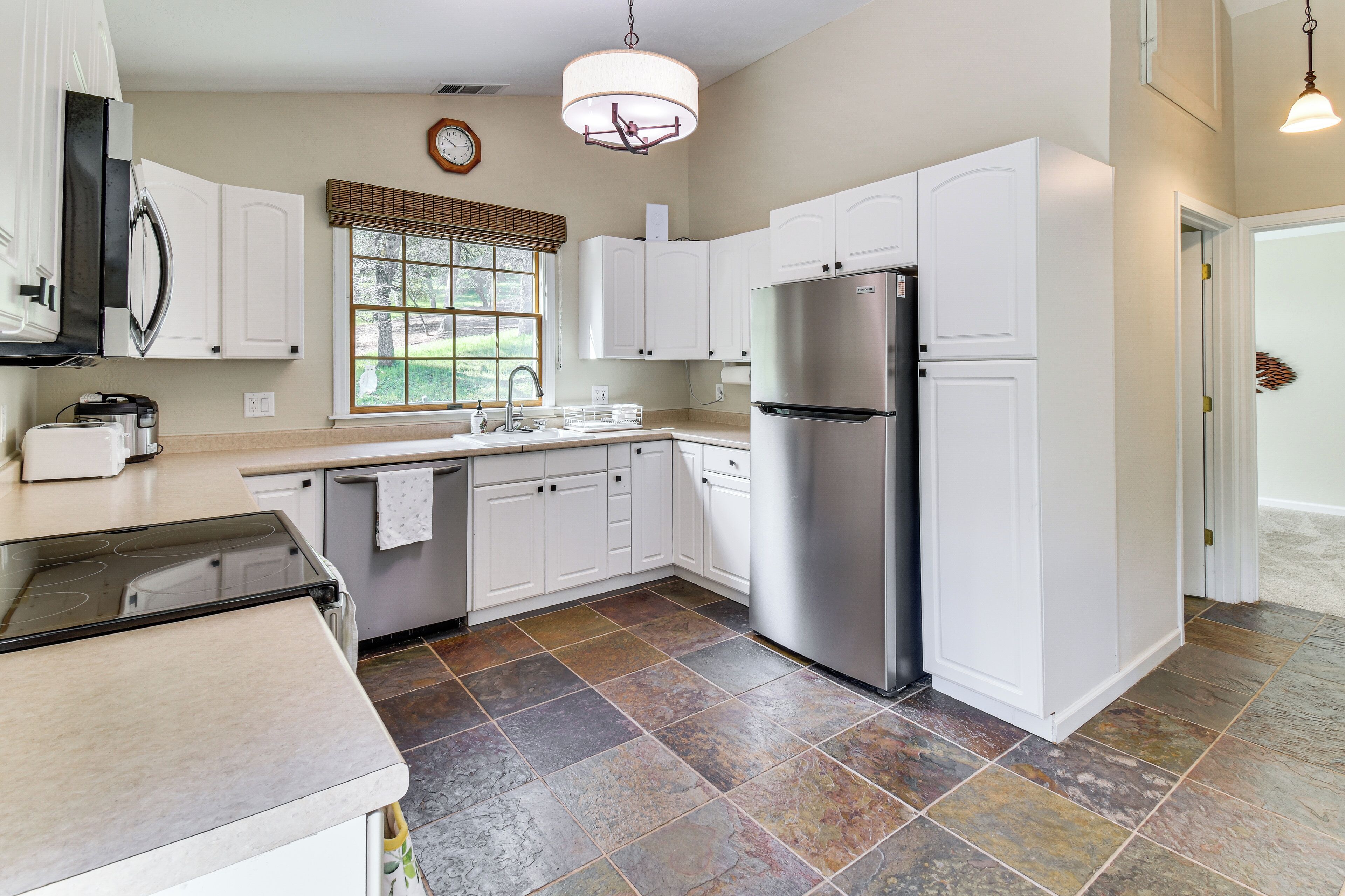A modern kitchen with white cabinets, a stainless steel refrigerator, and a window with blinds.