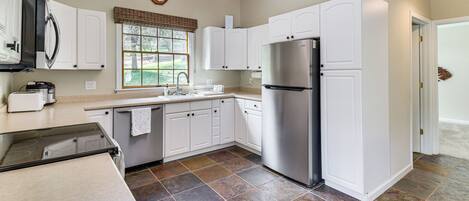 A modern kitchen with white cabinets, a stainless steel refrigerator, and a window with blinds.
