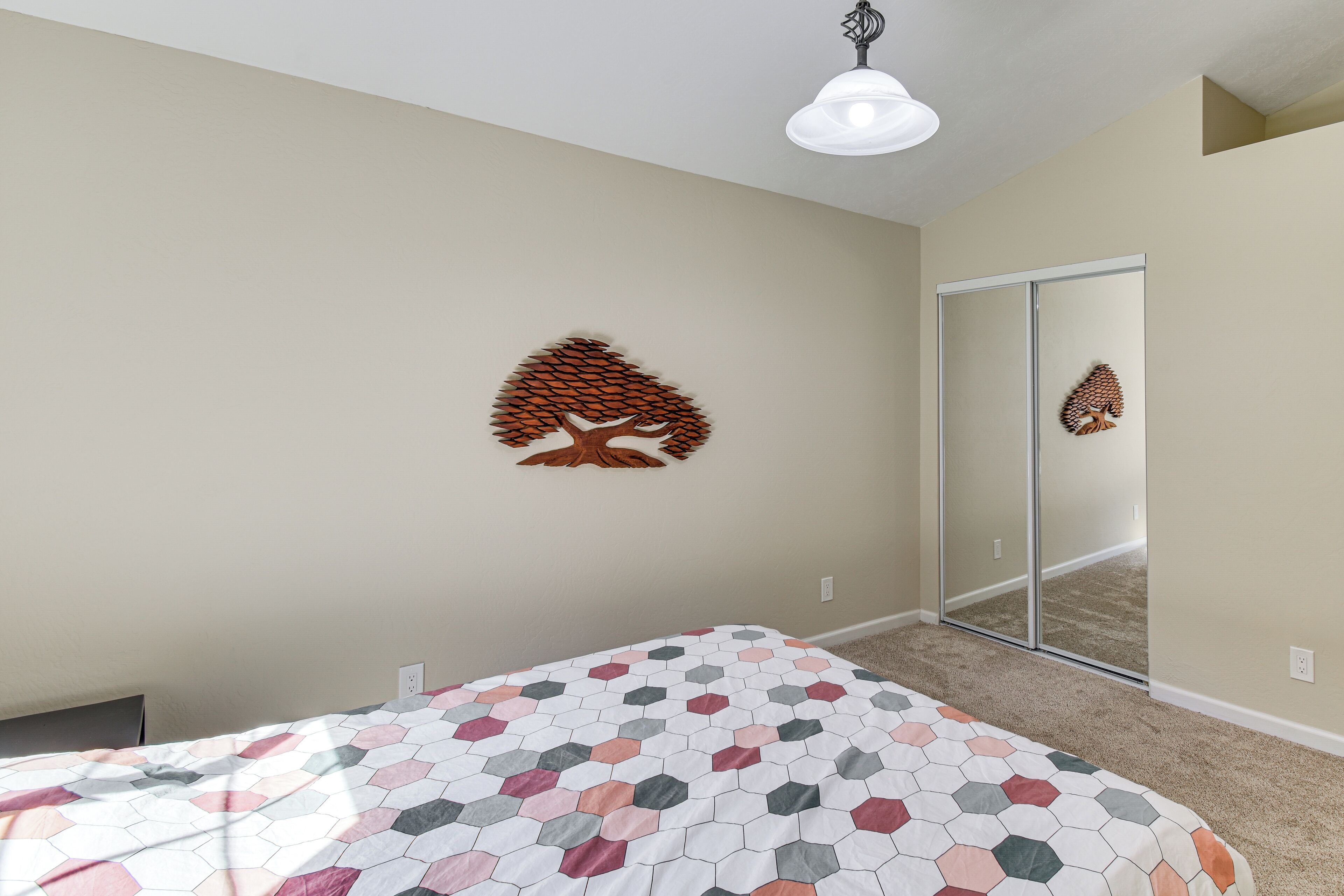 A bedroom with a bed, a wall-mounted tree decoration, a sliding glass door, and a ceiling light fixture.