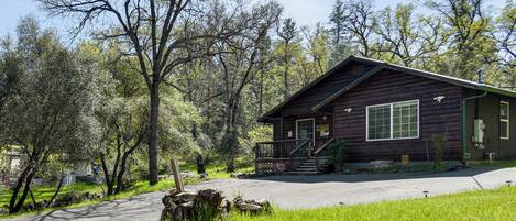 A rustic cabin with a porch, surrounded by trees and a clear sky.