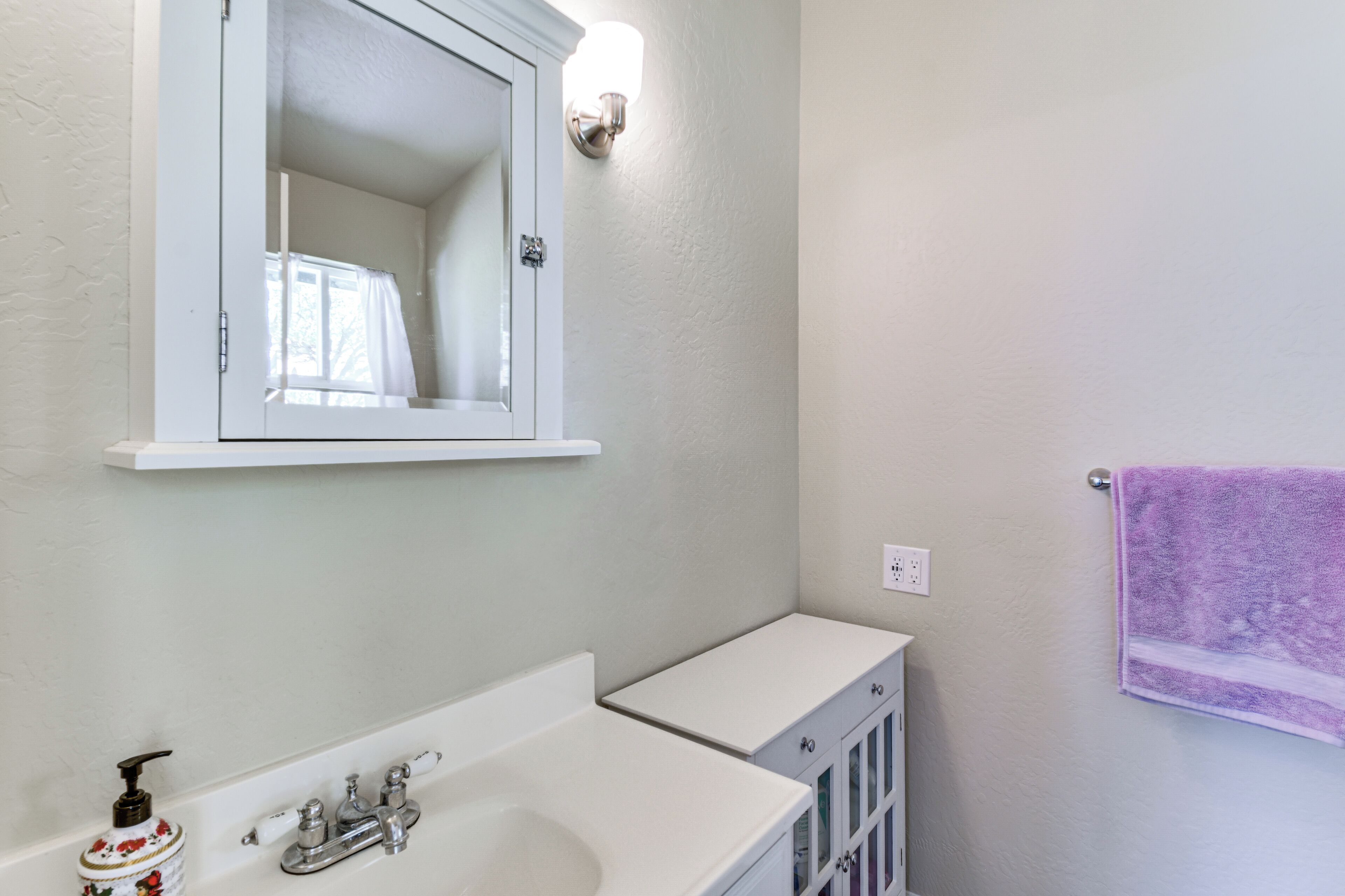 A bathroom with a white sink, a mirror, a purple towel, and a light fixture.