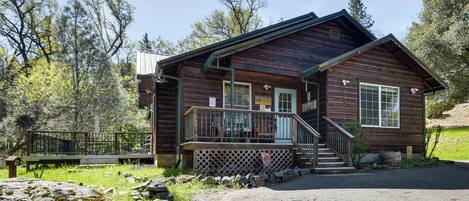 A wooden cabin with a porch, a staircase, and a fenced area.
