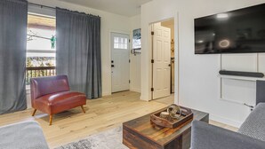 Un salon comprenant un fauteuil en cuir, une table basse en bois, un canapé gris et un téléviseur à écran plat fixé au mur.