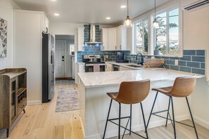 A modern kitchen with white cabinets, a marble island, and two bar stools.