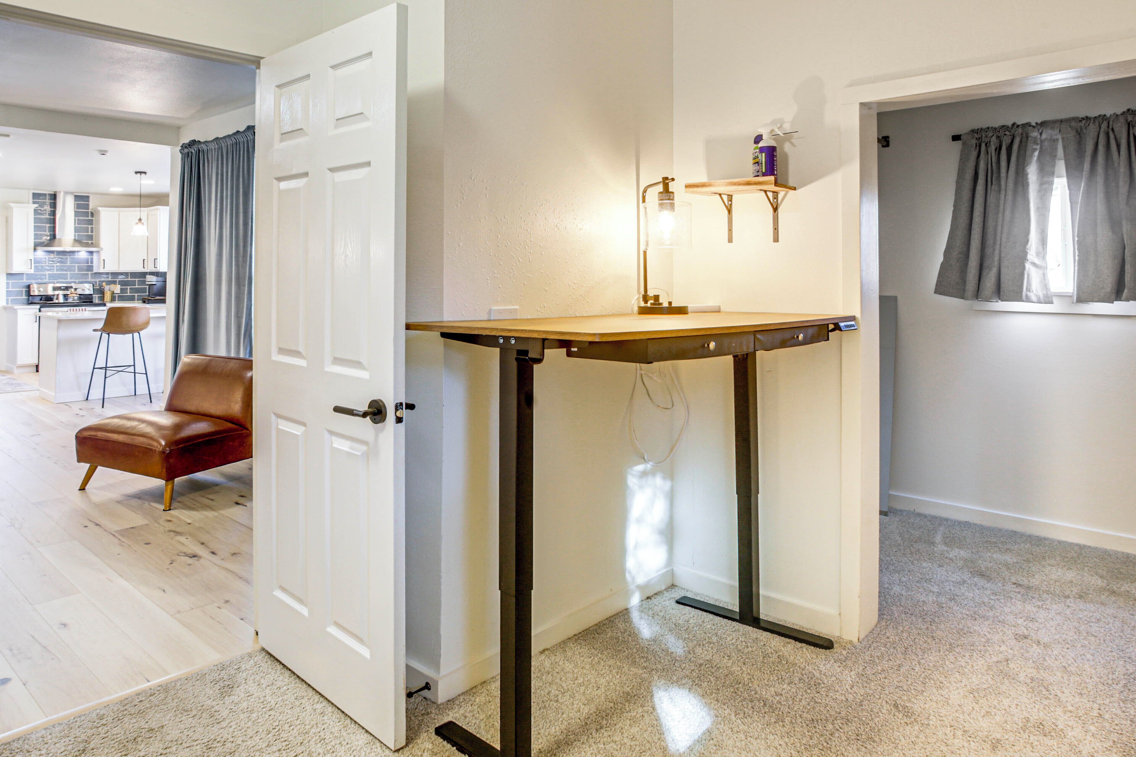 Una habitación con una puerta, una mesa con una lámpara, una silla y una ventana con cortinas.