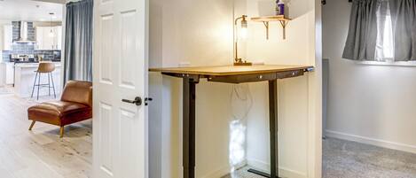 Una habitación con una puerta, una mesa con una lámpara, una silla y una ventana con cortinas.